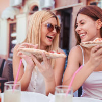 Pizza time. Young girls eating pizza in a cafe. Consumerism, lifestyle